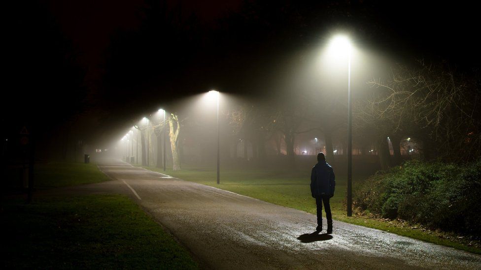 A silhouette of a person under a street lamp in a park