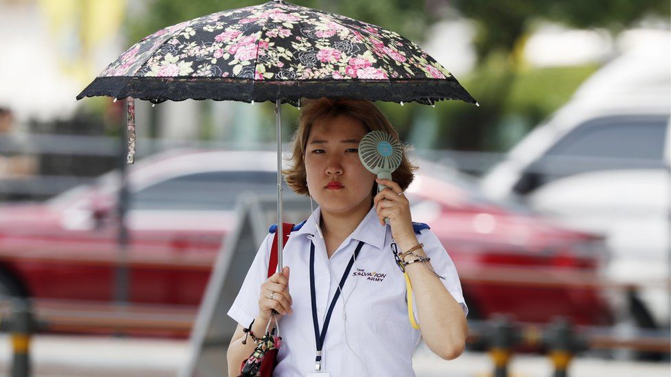 A South Korean woman holds a portable fan and an umbrella downtown in Seoul, South Korea, 24 July 2018.