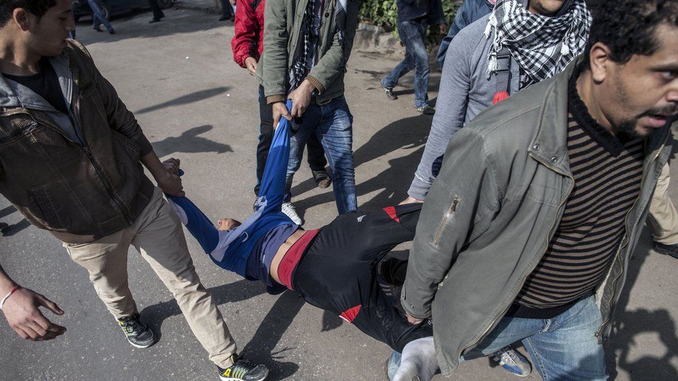 Egyptian anti-government protesters carry a person injured by a rubber bullet fired by police during clashes in Cairo on 25 January 2014