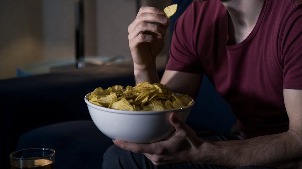 Stock photo of a bowl of delicious crisps illuminated by the glow of a living room television