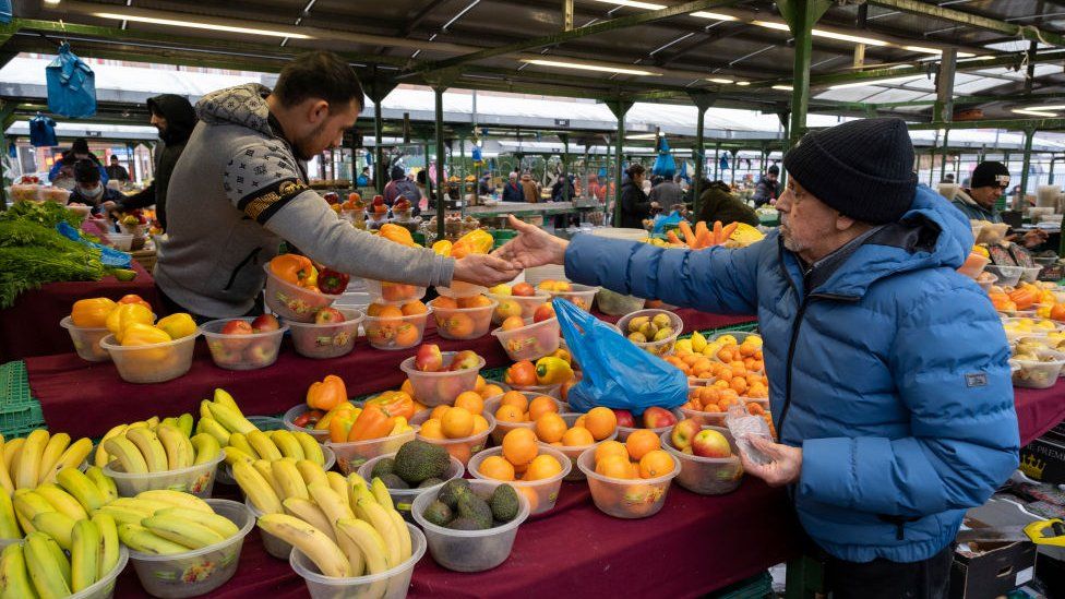 Stallholder serving his customers as they go shopping for fruit and vegetables at Birmingham Open Market