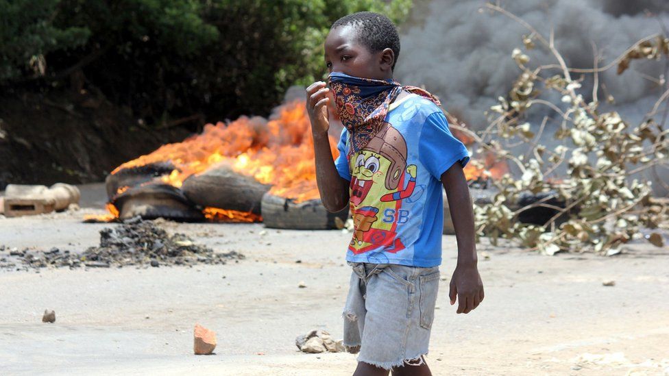 A child covers his mouth in Lusaka's Kanyama Township as he walks past a burning barricade of tyres on January 12, 2018, during clashes with protesters demonstrating against a curfew and a ban on street commerce imposed by the government in the wake of a cholera outbreak. Police in Zambia clashed on January 12 with residents in the capital Lusaka protesting an official ban on street commerce in a poor suburb intended to tackle a deadly cholera outbreak.