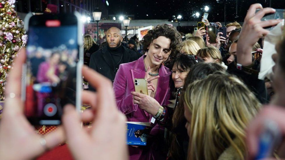 Timothee Chalamet takes selfies with fans as he arrives for the world premiere of Wonka at the Royal Festival Hall in London