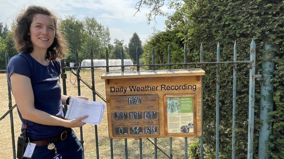 Katie Martyr standing in front of Cambridge University Botanic Garden's daily weather recording board