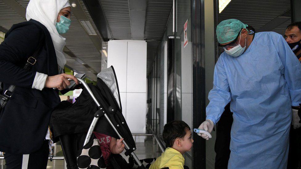 A health worker takes the temperature of a child at Damascus airport on 1 October 2020