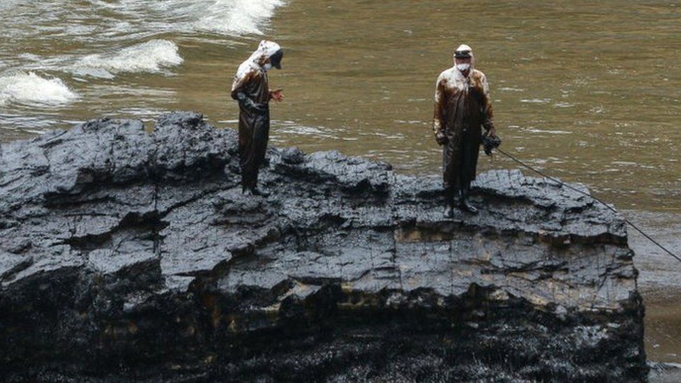 Repsol employees wearing biosafety suits work on the oil spill cleanup at the shore of Cavero Beach