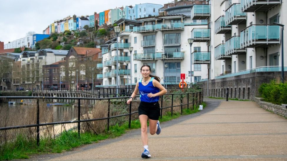 Ella runs by the harbour with Bristol's colourful houses behind her