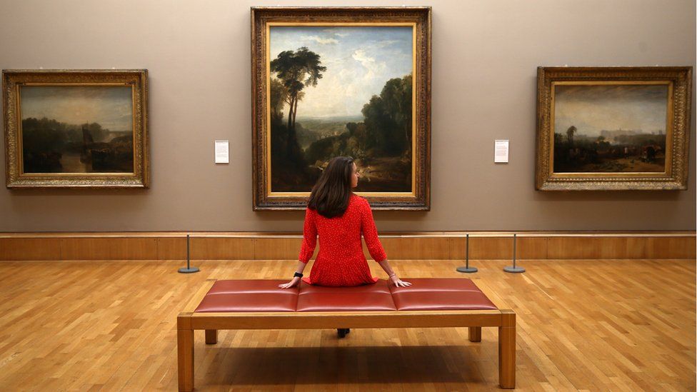 A gallery assistant poses amongst a selection of works by British artist JMW Turner at Tate Britain
