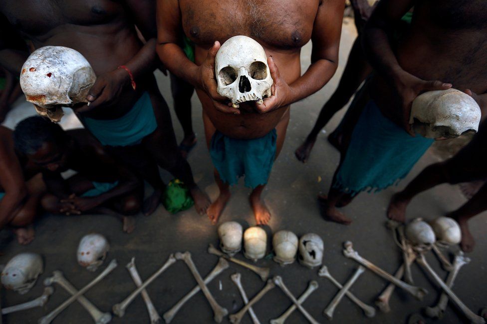 A row of men hold skulls.
