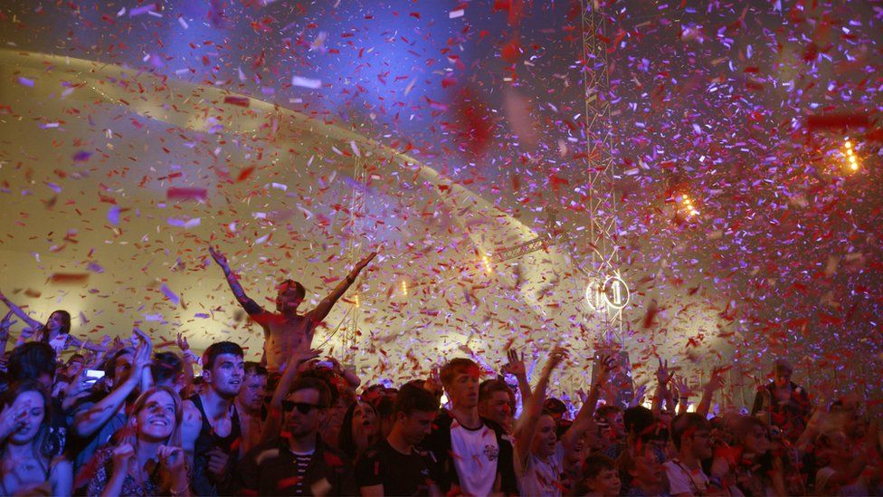 People in a crowd at a music gig cheering with confetti raining down on them