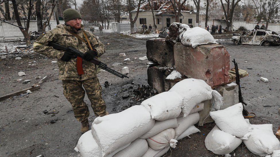 Ukrainian soldiers stand in the aftermath of an overnight shelling at the Ukrainian checkpoint near Kyiv