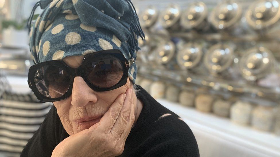 Wendy Whiteley cups her face while wearing a turban and big sunglasses