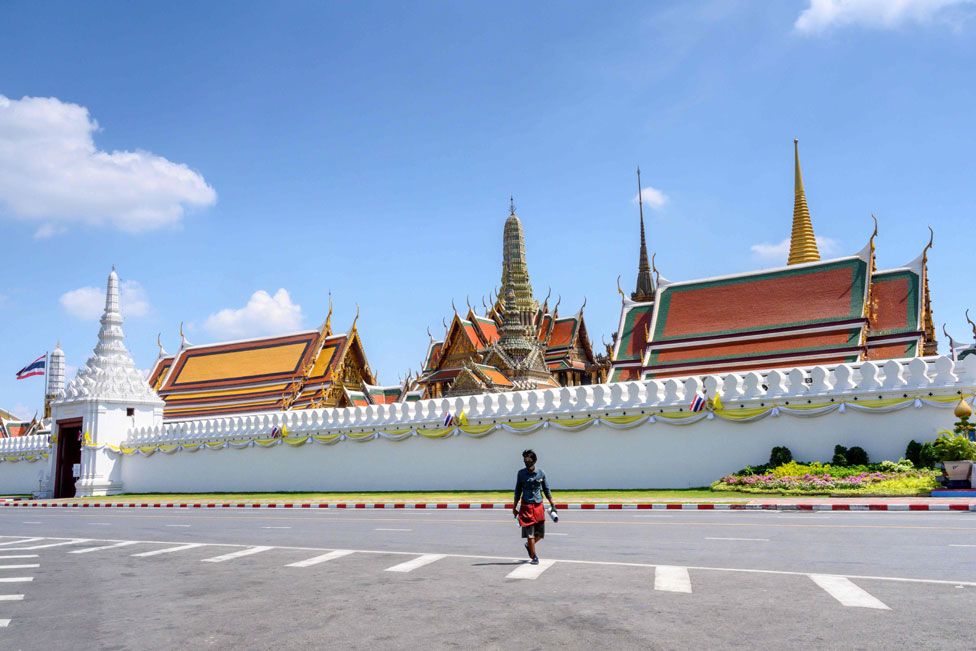 A man wearing a mask crosses a deserted street in front of the Grand Palace in Bangkok