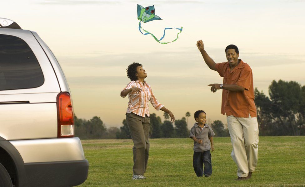 Family play with a kite next to car