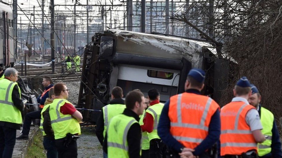 Rescuers and police officers stand next to the wreckage of the passenger train after it derailed (18 February 2017)