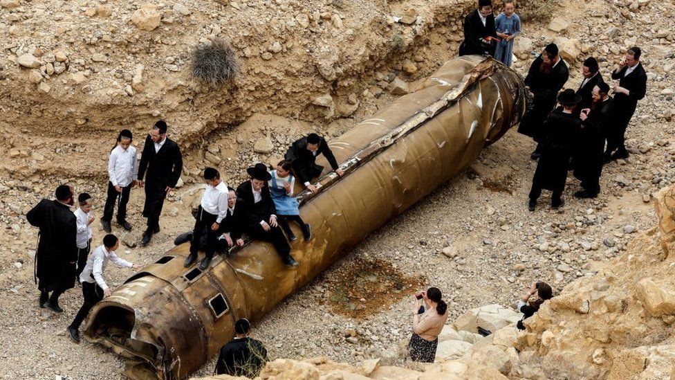 Israelis hang around the apparent remains of a ballistic missile in southern Israel, 26 April