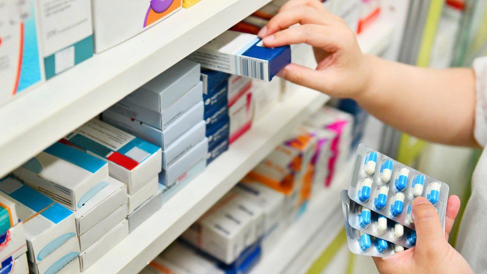 A pharmacist lifts a box of medicine off a shelf
