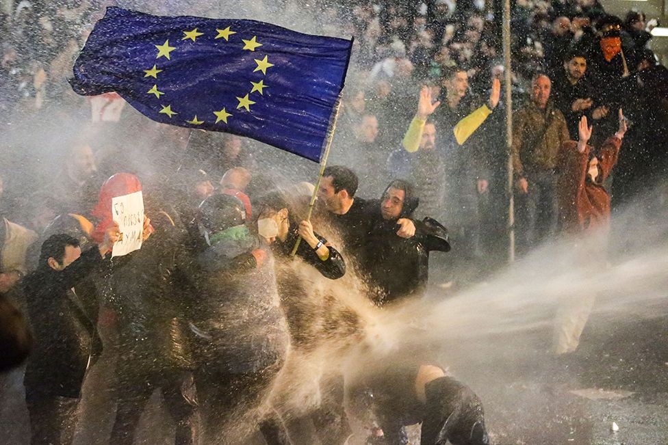 Protesters brandishing a European Union flag brace as they are sprayed by a water cannon during clashes with riot police near the Georgian parliament in Tbilisi