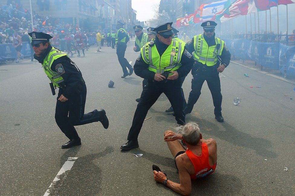 Police officers with their guns drawn hear the second explosion down the street. The first explosion knocked down 78-year-old US marathon runner Bill Iffrig at the finish line of the 117th Boston Marathon.