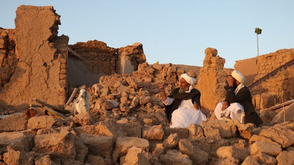 Afghan residents sit at a damaged house after earthquake in Sarbuland village of Zendeh Jan, district of Herat province