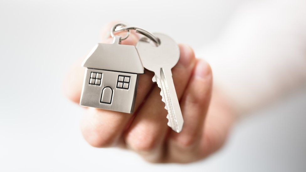 A hand holds a door key with a key fob of a house attached