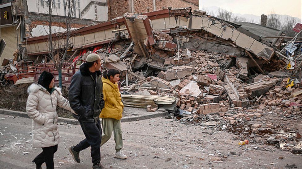 People walk past a collapsed building after an earthquake in Dahejia, Jishishan