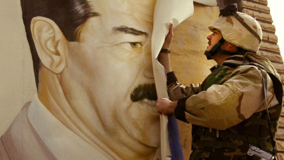 A US army officer rips down a poster of Saddam Hussein in Iraq in 2003