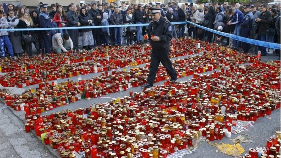 A Romanian policeman walks over a carpet of burning candles as he places flowers and candles left in respect for the club blaze victims, in front of the fire site, in Bucharest, Romania, 2 November 2015.
