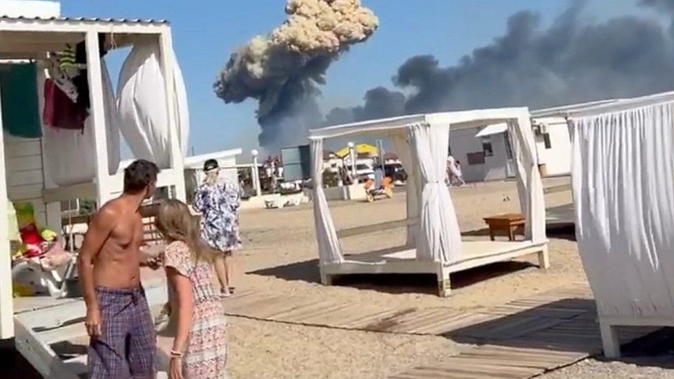 People on beach in Crimea, plume of smoke in background