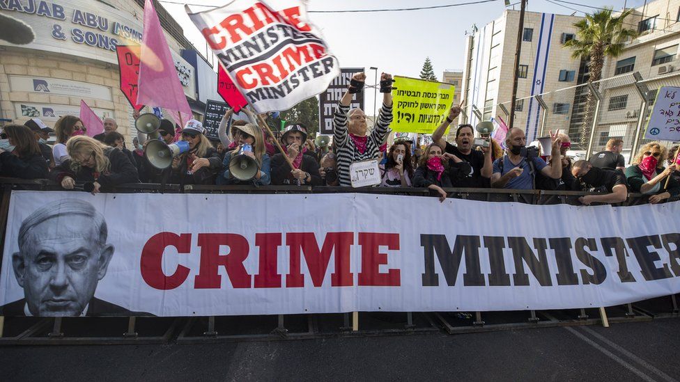 Protesters hold up a banner saying "crime minister" near the Jerusalem court ahead of the resumption of Benjamin Netanyahu's corruption trial (5 April 2021)