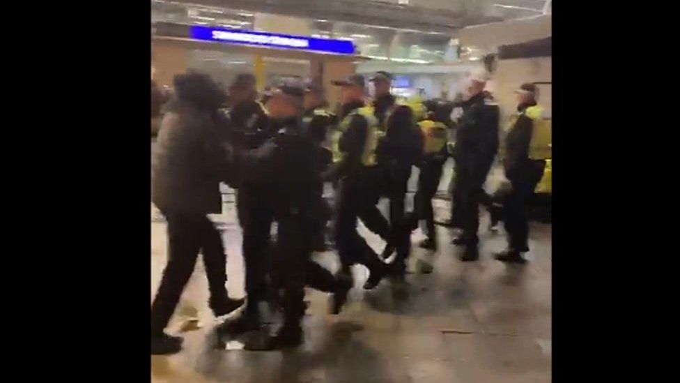 Still from a social media video showing police officers pushing back a man dressed in black with his hood up