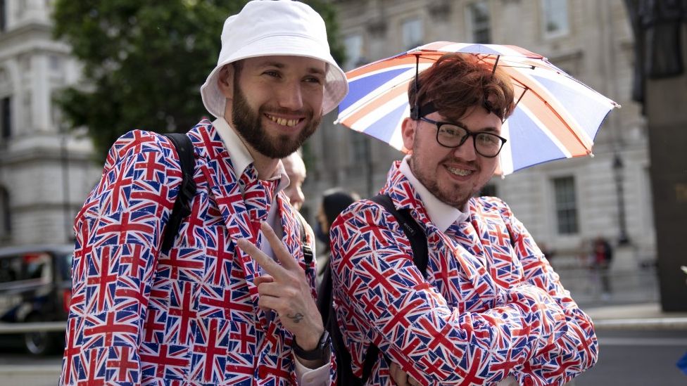 Two young men look pose for the camera wearing matching Union Jack suits.