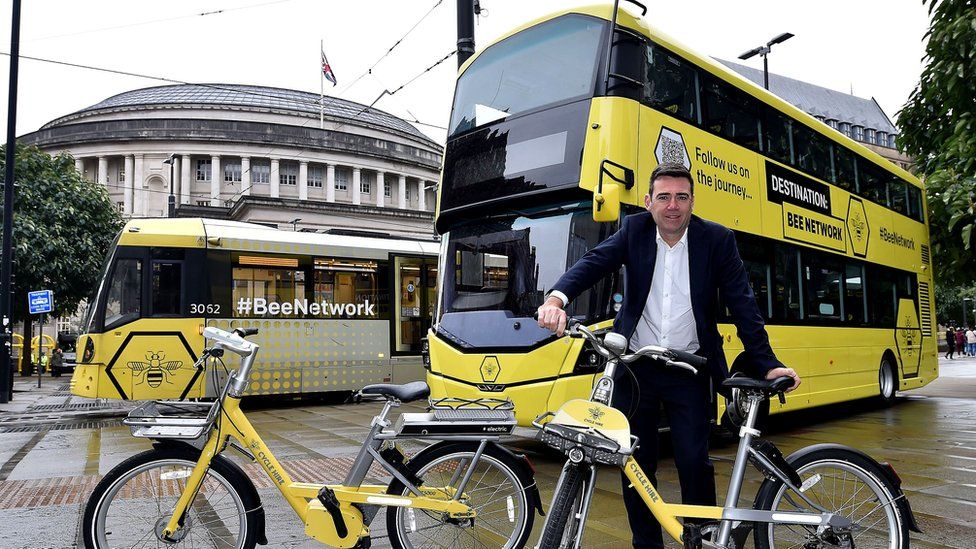 Andy Burnham with Bee Network bikes, bus and tram outside the Central Library in Manchester