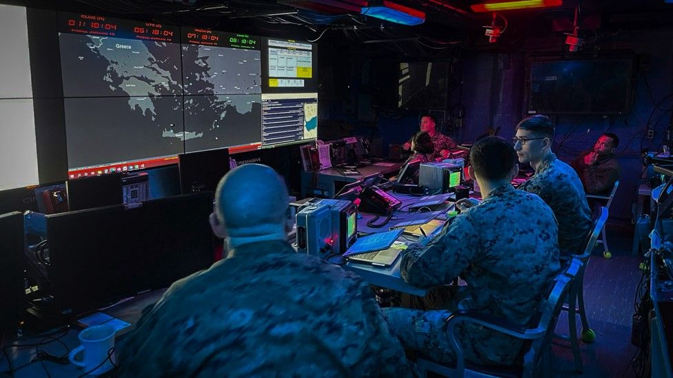 A group of people sit in front of digital map in a command centre