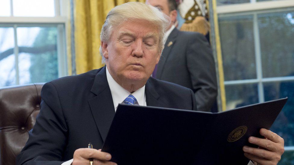 US President Donald Trump reads an executive order withdrawing the US from the Trans-Pacific Partnership prior to signing it in the Oval Office of the White House in Washington, DC, January 23, 2017