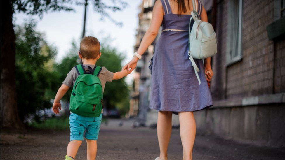 Woman and boy walk away holding hands