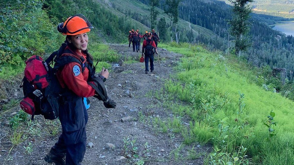 Devyn Gale, a young firefighter killed while tackling wildfires in Canada, is seen standing on a footpath on a mountainside in her firefighters' uniform. She is sticking out her tongue.