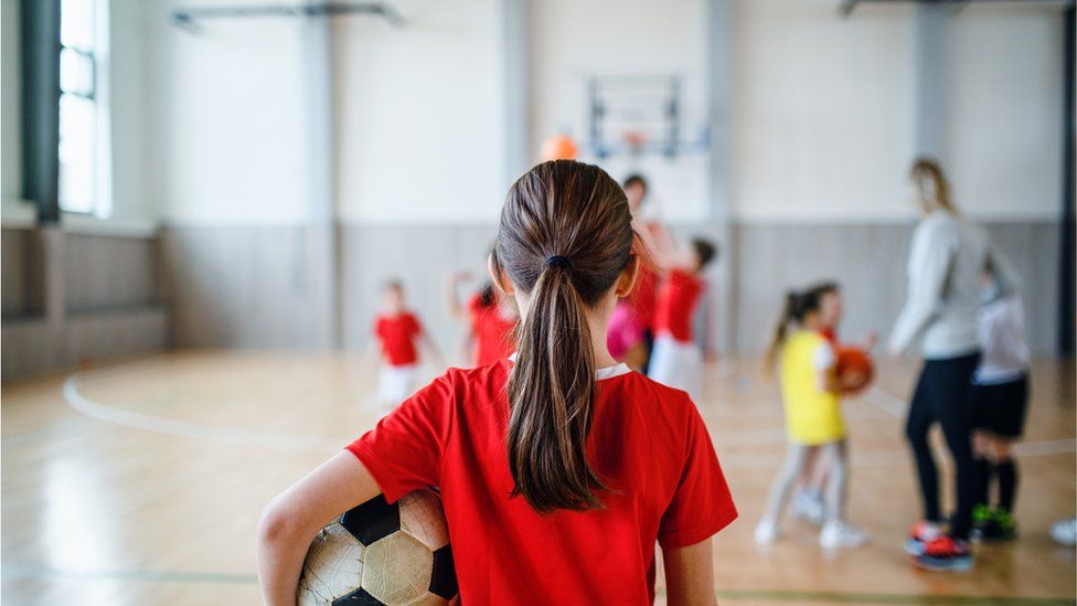 Девушка держит мяч на школьном уроке спорта