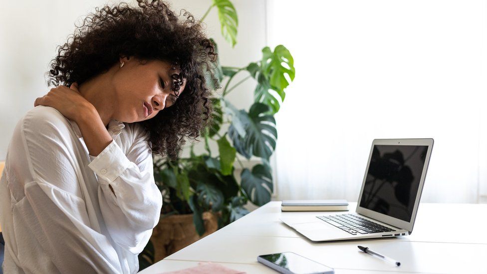 A person massaging pain in her shoulder while sat at a laptop