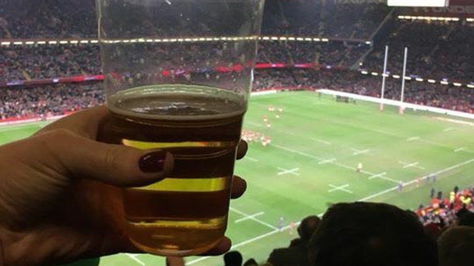 A woman holding a beer while watching a Wales rugby match
