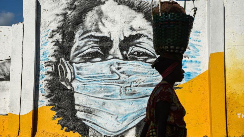 A Tanzanian woman carries a basket on her head as she walks in front of a graffiti painted by the Wachata artists group to raise awareness about wearing masks to avoid the risk of Covid-19 in Dar es Salaam on26 May 2020