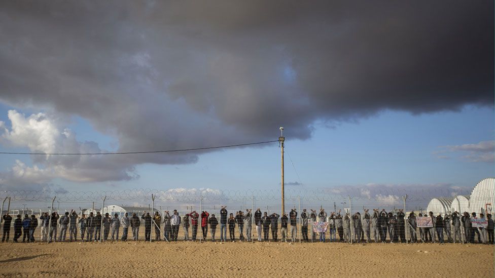 Asylum seekers stage a protest by leaning against the fence of the Holot detention centre