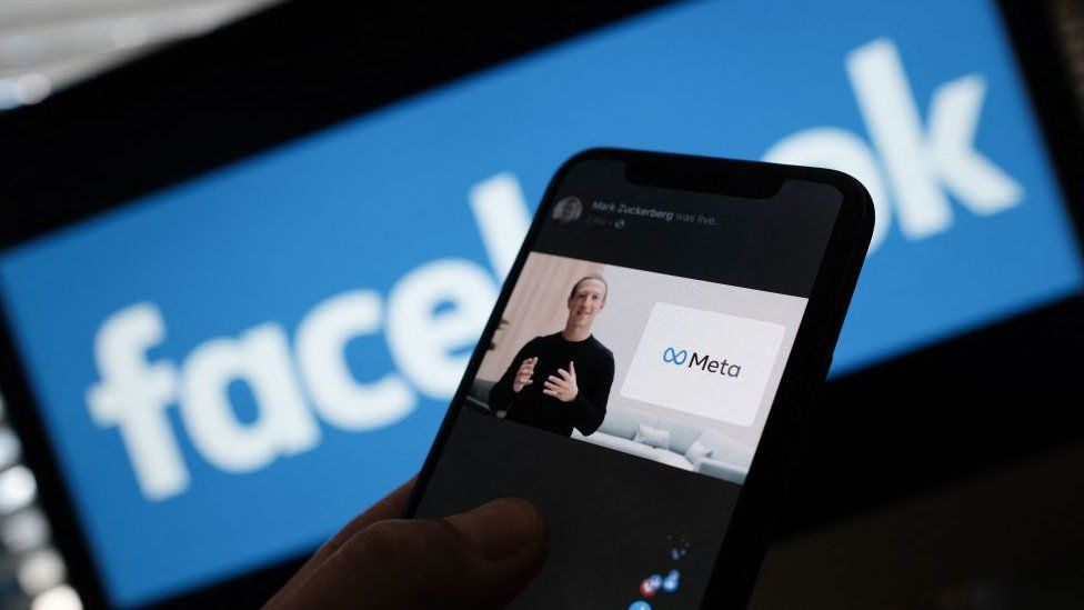 Mark Zuckerberg and meta logo shown on a phone screen with facebook logo in the background in a stock illustration