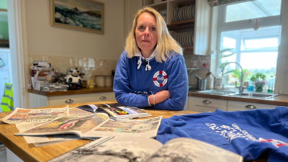 Bryony Sadler wearing her FLAG campaign hoodie, with some of the hundreds of press reports covering her work in 2014