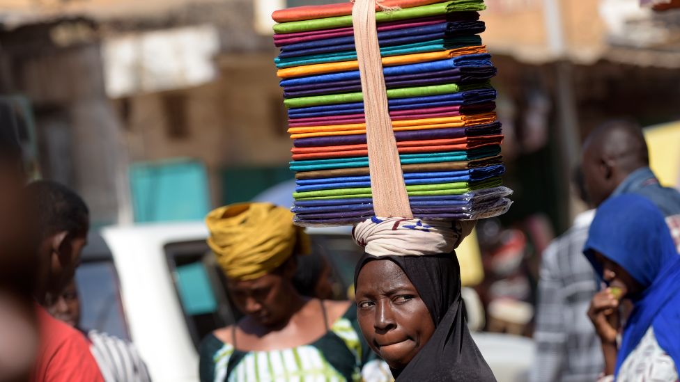 A seller carries folded fabric on her head through the Serrekunda marketplace in The Gambia - 2016