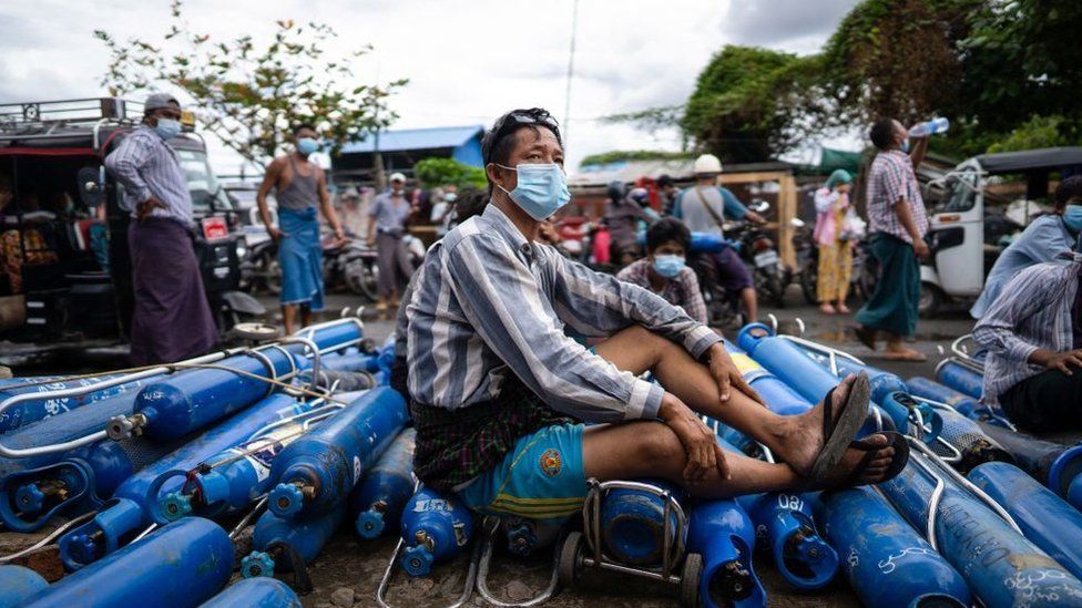 A man sits on empty oxygen canisters in Mandalay