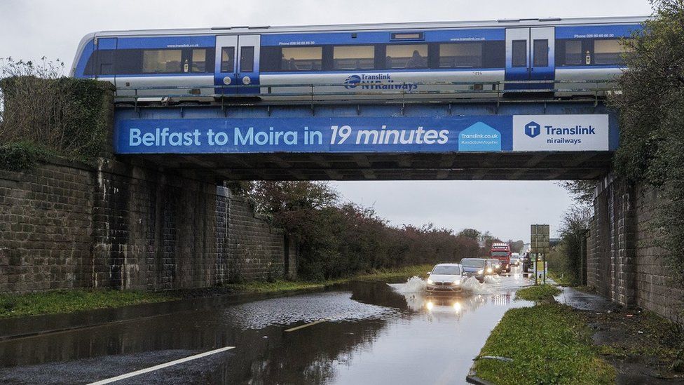 Cars approach a flooded road under a railway bridge