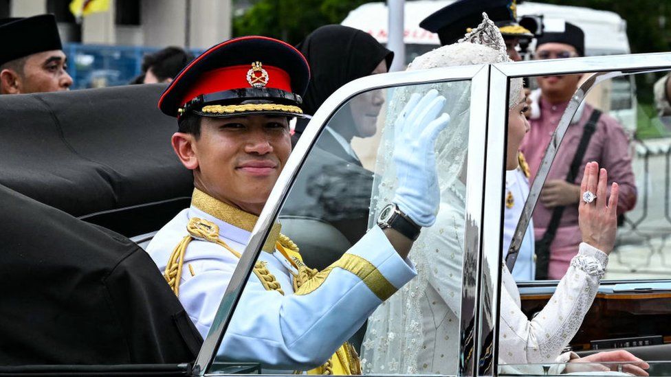 Prince Abdul Mateen and Yang Mulia Anisha Rosnah wave from their car during the wedding procession in Brunei's capital Bandar Seri Begawan on January 14, 2024.