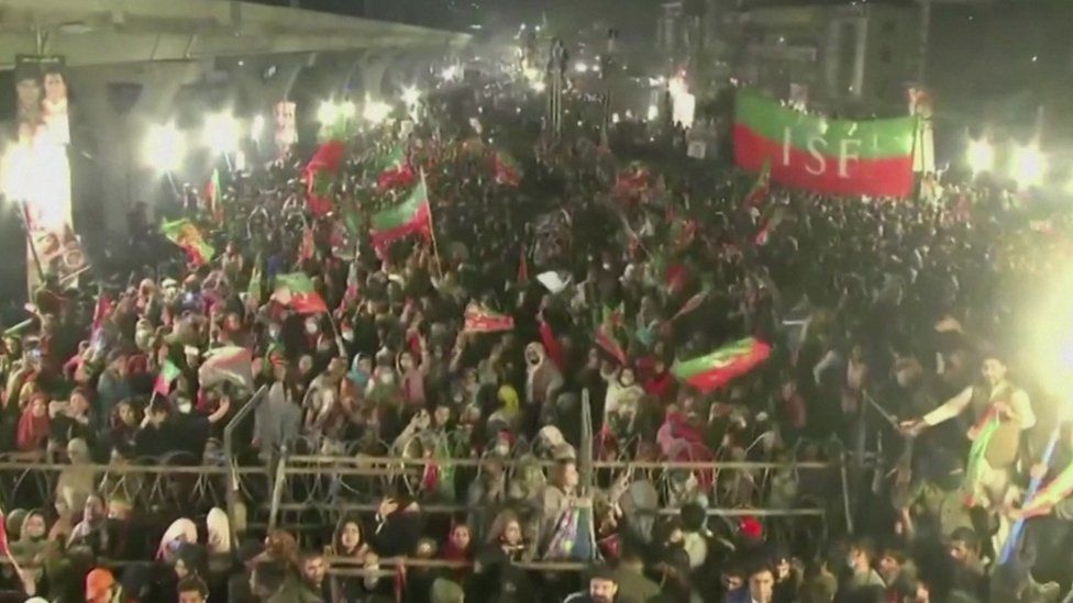 A large gathering of Imran Khan's supporters, some of whom wave flags and banners