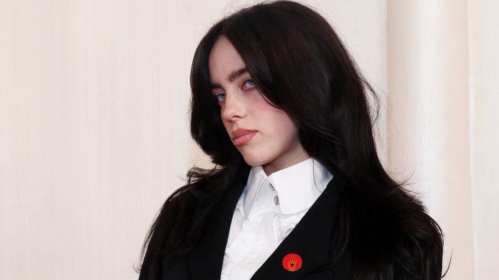 Billie Eilish at the 86th Academy Awards, wearing a black suit jacket with a white shirt and a red pin